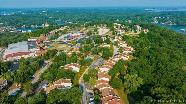 aerial view of property and surrounding area featuring a forest and a nearby body of water