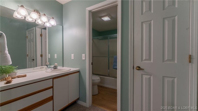 full bathroom featuring toilet, vanity, shower / bath combination with glass door, and baseboards
