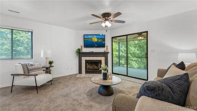 living room with carpet flooring, a ceiling fan, a tile fireplace, and baseboards