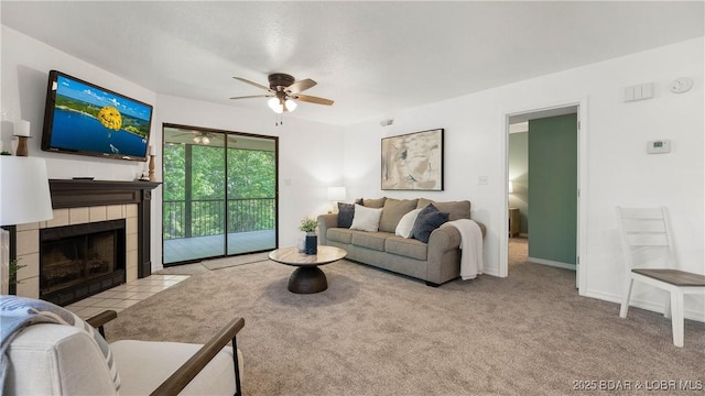living room featuring carpet floors, ceiling fan, a tiled fireplace, and baseboards
