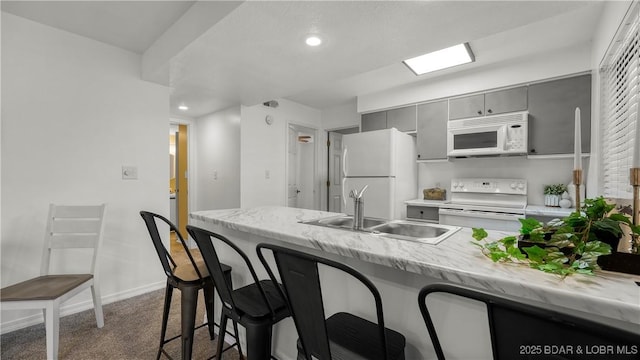 kitchen featuring white appliances, gray cabinets, a sink, a kitchen breakfast bar, and recessed lighting