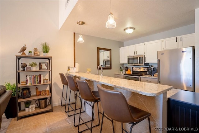 kitchen featuring stainless steel appliances, a peninsula, a kitchen breakfast bar, white cabinets, and light stone counters
