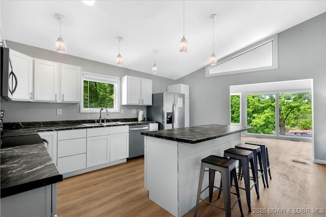 kitchen featuring appliances with stainless steel finishes, lofted ceiling, a sink, a breakfast bar area, and light wood-style floors