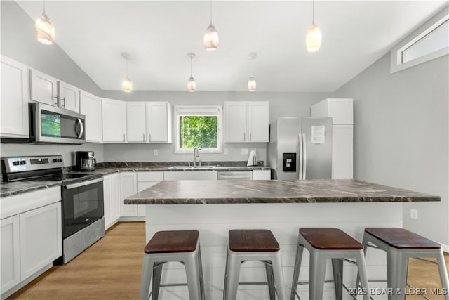 kitchen with stainless steel appliances, lofted ceiling, a breakfast bar area, a sink, and white cabinets