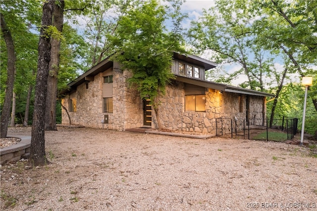 back of property featuring stone siding and fence