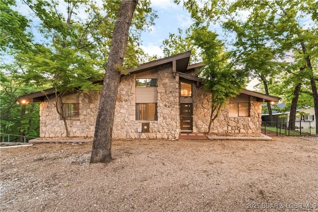 rear view of property with stone siding and fence