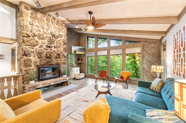 living room with ceiling fan, a stone fireplace, a textured ceiling, and wood finished floors