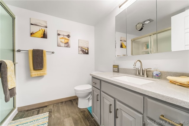 full bath featuring wood finished floors, vanity, toilet, a shower with door, and baseboards