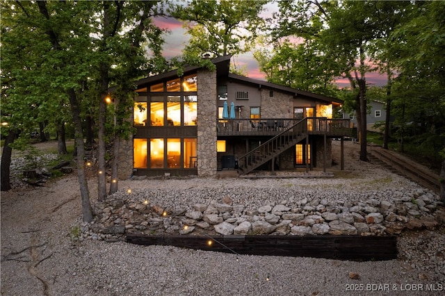 back of house at dusk with stone siding, stairs, and a wooden deck