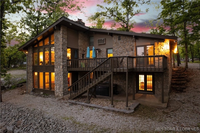 back of property at dusk with stone siding, a deck, stairway, a patio area, and a chimney