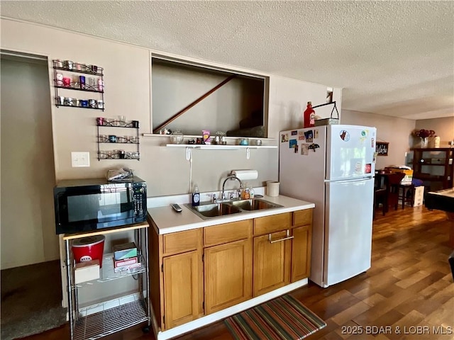kitchen with black microwave, freestanding refrigerator, a sink, a textured ceiling, and light countertops