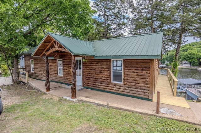 view of front facade featuring metal roof, a water view, log siding, and a patio area