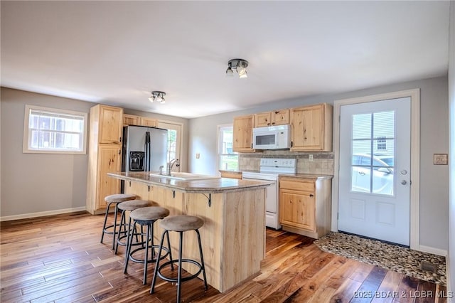 kitchen featuring white appliances, light brown cabinetry, a kitchen breakfast bar, and a sink