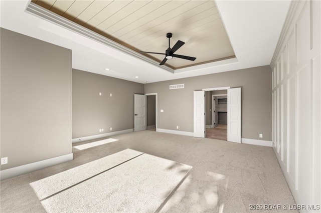 unfurnished bedroom featuring a raised ceiling, light carpet, wooden ceiling, baseboards, and ceiling fan