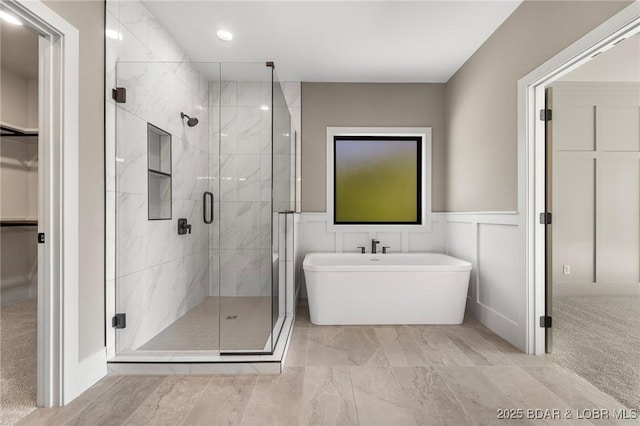 bathroom with a spacious closet, a shower stall, a freestanding tub, marble finish floors, and a wainscoted wall