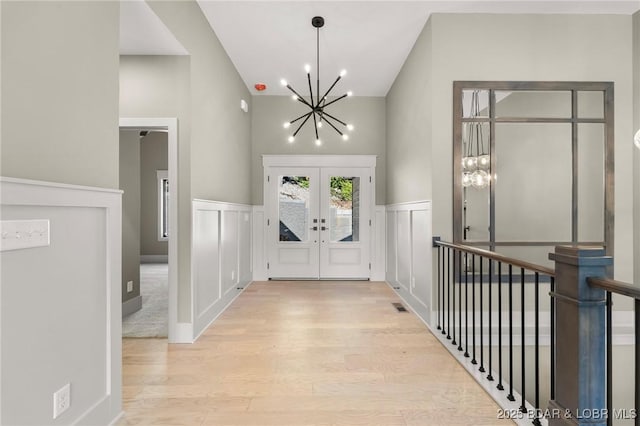 foyer featuring a chandelier, wood finished floors, french doors, wainscoting, and a decorative wall