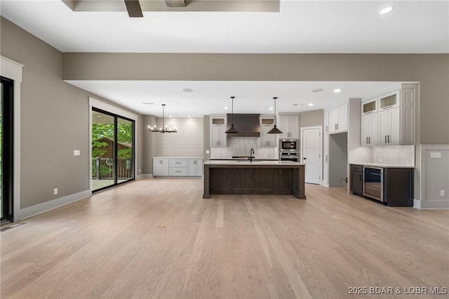 kitchen featuring beverage cooler, stainless steel appliances, light wood-style floors, backsplash, and extractor fan