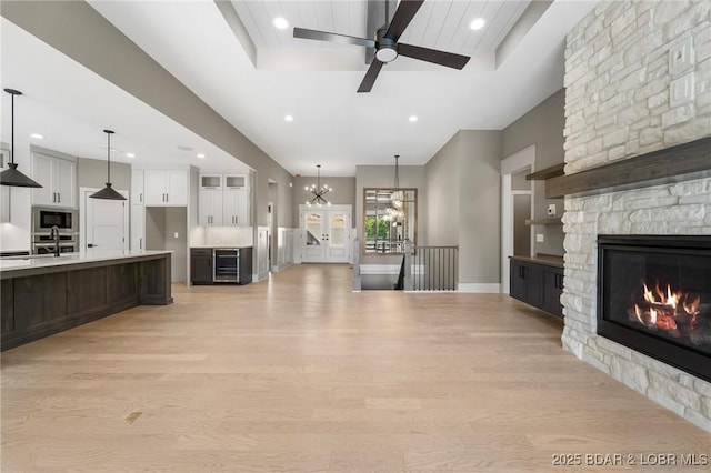 unfurnished living room featuring recessed lighting, a stone fireplace, ceiling fan, light wood-style flooring, and wine cooler