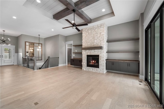 unfurnished living room featuring light wood-type flooring, a chandelier, a stone fireplace, beamed ceiling, and recessed lighting