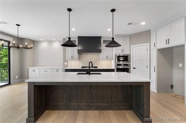 kitchen with a sink, premium range hood, white cabinetry, light wood-type flooring, and recessed lighting