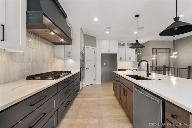 kitchen featuring appliances with stainless steel finishes, custom exhaust hood, a sink, white cabinetry, and light wood-style flooring