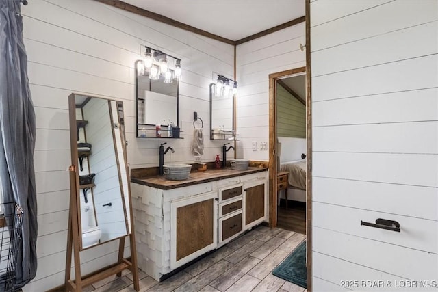 full bath with wood finished floors, double vanity, wooden walls, and crown molding