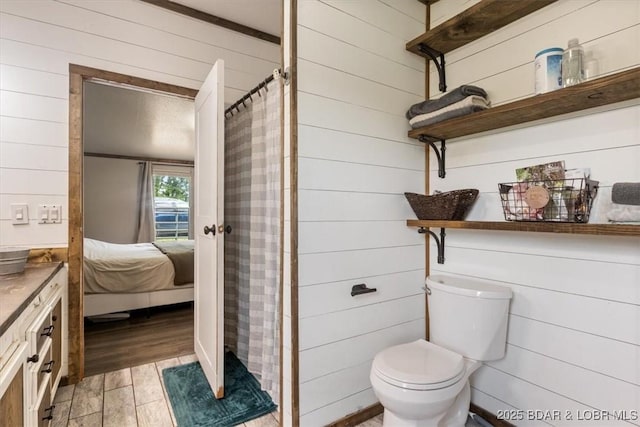 bathroom with wood walls, a shower with shower curtain, ensuite bathroom, toilet, and wood finished floors