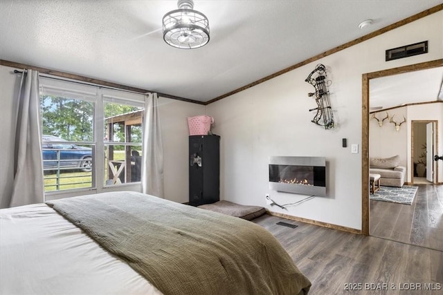 bedroom featuring a glass covered fireplace, ornamental molding, wood finished floors, heating unit, and baseboards