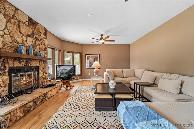 living room with light wood-style flooring, ceiling fan, and a stone fireplace