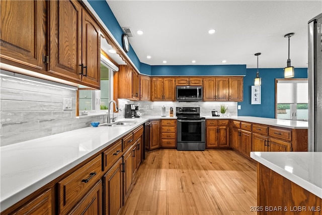 kitchen with stainless steel appliances, plenty of natural light, brown cabinetry, light wood-type flooring, and recessed lighting
