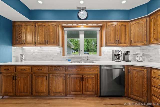kitchen featuring stainless steel dishwasher, a sink, brown cabinetry, and light countertops
