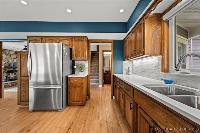 kitchen featuring freestanding refrigerator, a sink, light wood-type flooring, brown cabinets, and light countertops