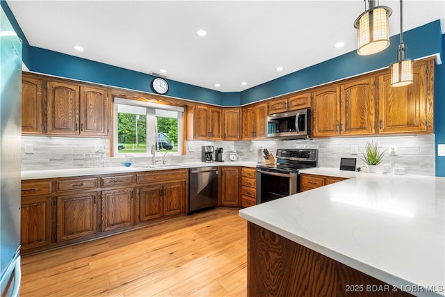 kitchen with stainless steel appliances, a sink, brown cabinetry, light wood finished floors, and recessed lighting