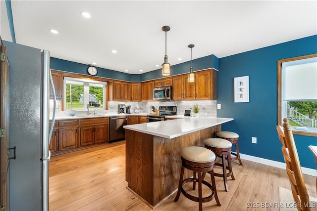 kitchen with appliances with stainless steel finishes, a peninsula, brown cabinetry, a kitchen breakfast bar, and recessed lighting