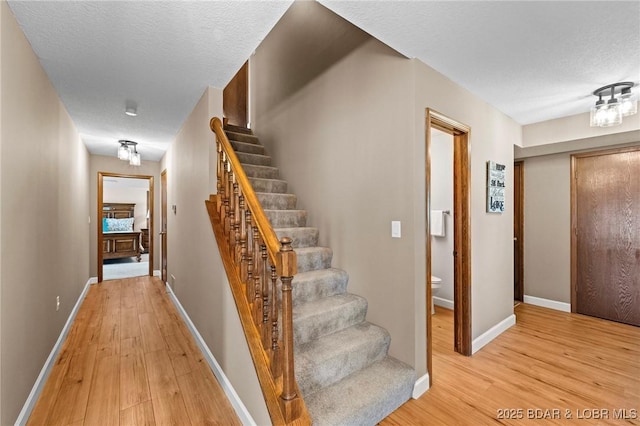stairs with wood finished floors, baseboards, and a textured ceiling