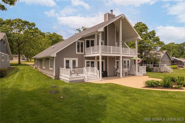 rear view of house with a balcony, a patio, a chimney, a deck, and a lawn