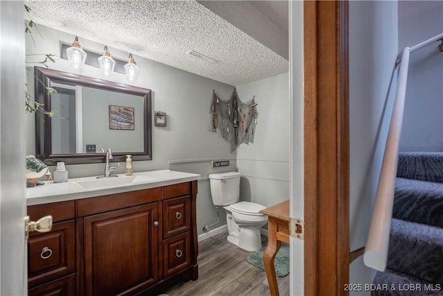 ensuite bathroom featuring toilet, wood finished floors, vanity, and a textured ceiling