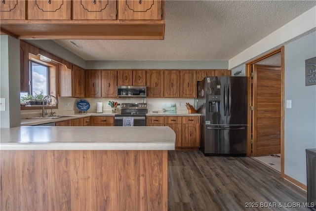 kitchen featuring stainless steel appliances, a sink, brown cabinets, light countertops, and a peninsula