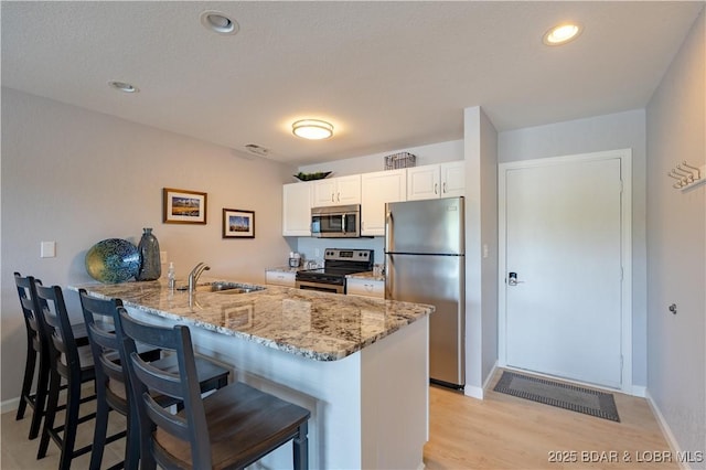 kitchen featuring appliances with stainless steel finishes, a sink, a kitchen bar, a peninsula, and light stone countertops