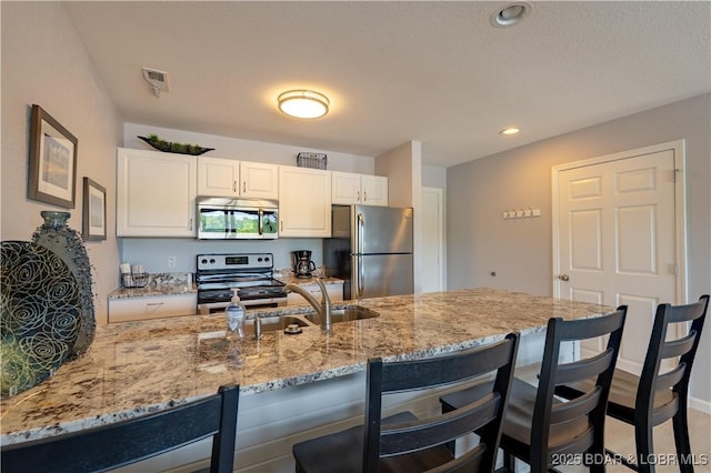 kitchen featuring stainless steel appliances, a kitchen breakfast bar, light stone counters, a sink, and white cabinetry