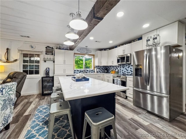 kitchen featuring appliances with stainless steel finishes, beverage cooler, a center island, white cabinets, and backsplash