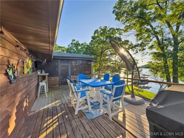wooden terrace featuring a sunroom, a water view, outdoor dining area, and area for grilling