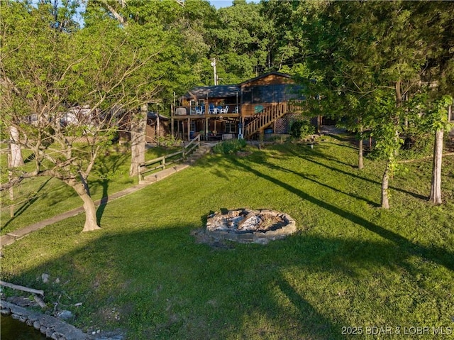 view of grassy yard featuring stairway, a deck, an outdoor fire pit, and a wooded view