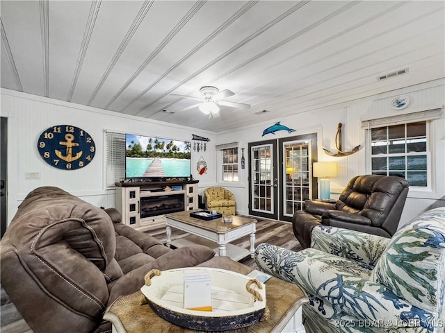 living room with french doors, wood finished floors, a ceiling fan, and wood walls