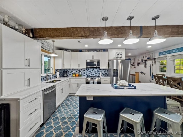 kitchen featuring stainless steel appliances, a sink, a kitchen breakfast bar, white cabinets, and a kitchen island