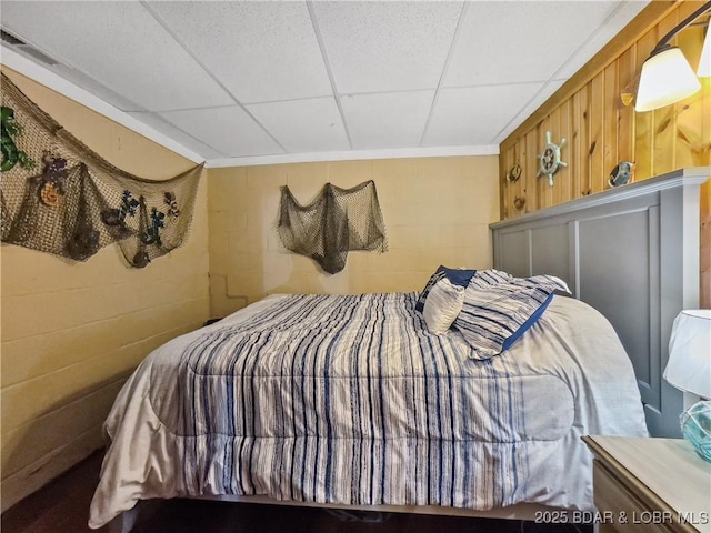 bedroom with concrete block wall and a paneled ceiling