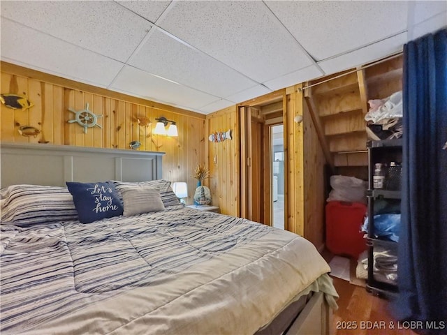 bedroom with wood finished floors, wooden walls, and a drop ceiling