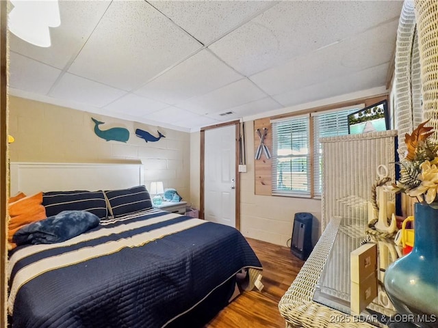 bedroom with wood finished floors, concrete block wall, and a paneled ceiling