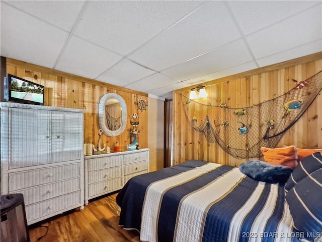 bedroom with wood walls, a paneled ceiling, and wood finished floors