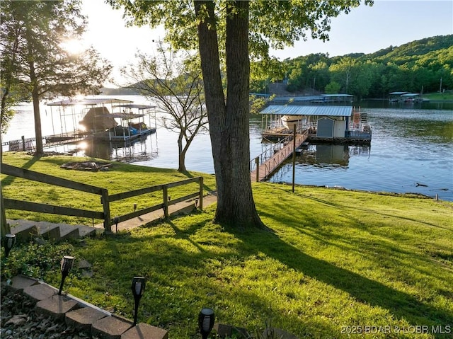 dock area featuring a water view, boat lift, a lawn, and a forest view